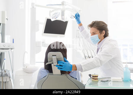 Young handsome dentist doctor comforting female patient sitting in dentist chair, copy space Stock Photo