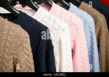 Various cable knit sweaters or pullovers on hanger rack in a clothes store or at a wardrobe, selective focus Stock Photo