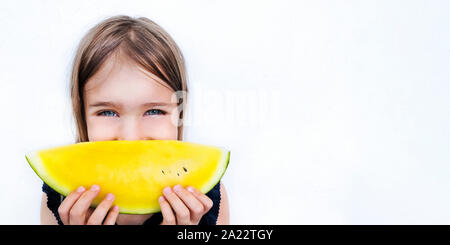 Happy girl holding watermelon slice close up. Smiling child eating yellow fruit. Healthy nutrition, organic summer product concept. Kid with cheerful Stock Photo