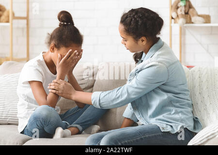 Upset african little girl being consoled by her elder sister, home interior Stock Photo
