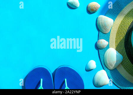 Blue flip-flops, colorful striped hat and sea shells on turquoise background with copy space. Holiday by the beach. Beach accessories Stock Photo