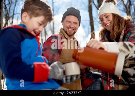 Family of a mother, father and boy child having fun and sharing a cup of cocoa and chocolate chip cookies in snow during the winter season Stock Photo