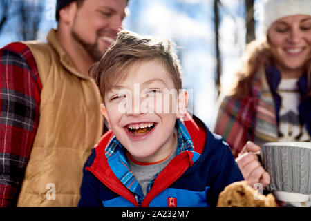 Family of a mother, father and boy child having fun and sharing a cup of cocoa and chocolate chip cookies in snow during the winter season Stock Photo