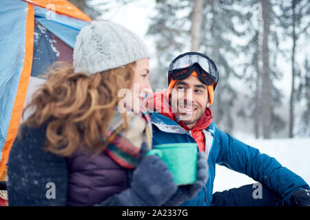 Diverse couple of indian guy and caucasian woman setting camp with a tent in a snow filles canadian park during a snowshoeing trip Stock Photo