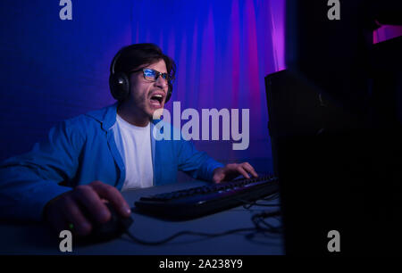 Emotional gamer playing video game online and shouting, wearing headset and glasses Stock Photo