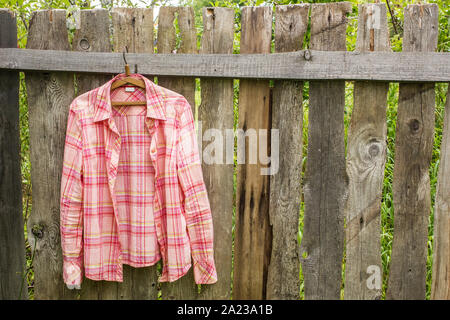 Shirt hangs a on hanger on the old fence of outdoors the boards in a village Stock Photo