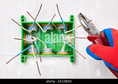 Electrical services. Installation of a rectangular electrical junction box made of green plastic on the wall of a house. An electrician uses pliers to Stock Photo