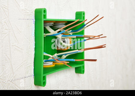 Wall-mounted installation of a rectangular plastic electrical junction box for household wiring. Insulation was removed from the ends of the copper wi Stock Photo