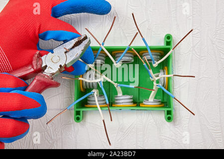 Installation of a rectangular electrical distribution box made of green plastic, on the wall of a residential building. The installer uses pliers to c Stock Photo