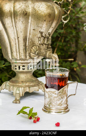 vintage copper samovar in a cup holder and a glass of hot tea close-up stands on the table beside are scattered fresh berries in a Russian village out Stock Photo