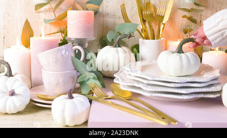 Thanksgiving Autumn Fall modern stylish table setting in new season colours, blush pink and white theme, stacked on service sideboard, setting up. Stock Photo