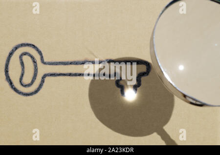 Focus is key (one key version), illustrated by using magnifying glass to focus sunlight to create key shaped burn mark on piece of brown paper Stock Photo