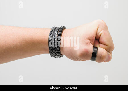 Punch hand. Hand of a white man wearing black accessories with a closed fist giving a punch. Side view, white background. Stock Photo