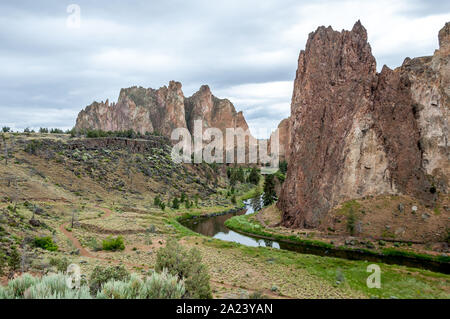 Crooked River winds through Smith Rock State Park in early summer, grass still green beside it and moody clouds above. Stock Photo