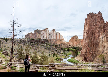 At Smith Rock State Park in Central Oregon, a woman hiker stops to take a photo of the steep rock faces towering above the river. Stock Photo