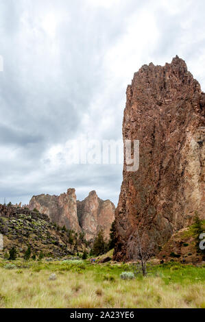 Smith Rock State Park with high cliffs of basalt and tuff, ideal for rock climbing. Vertical shot with moody sky, green grass below. Stock Photo