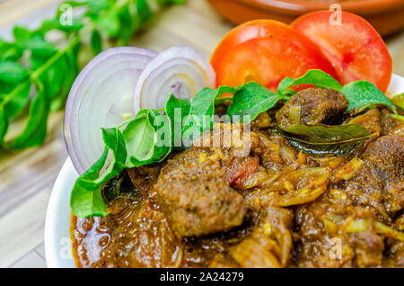 Closeup of spicy beef curry garnished with onions, curry leaves & tomato. Traditional South Indian (Kerala) cuisine. Stock Photo