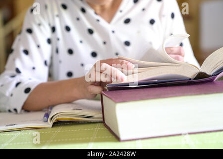 Woman studying for her assignment, flipping pages of a book while taking notes, Stock Photo
