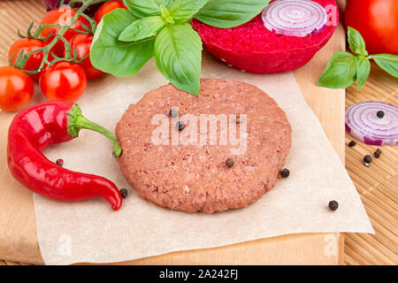 Vegan burger cooking with raw soy meat cutlet, seasoning and vegetables