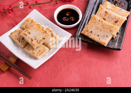 Chinese lunar new year food concept, Delicious turnip radish cake, local cuisine in restaurant with soy sauce on red background, close up, copy space Stock Photo