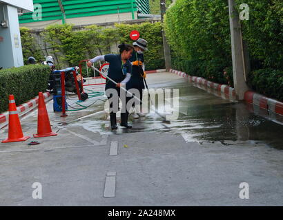 Bangkok, Thailand - September 28, 2019: Blurred motion of a female worker cleaning the floor with mop, while the other uses high pressure cleaner spra Stock Photo