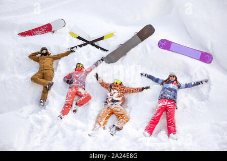 Four happy friends skiers and snowboarders are having fun and lying on snow with ski and snowboards. Aerial view Stock Photo