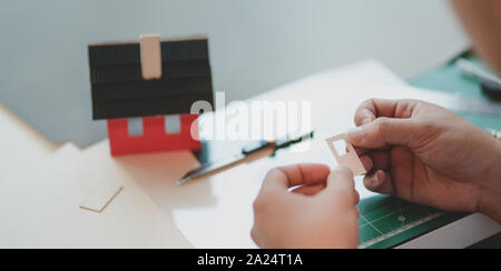 Close-up view of young male architect making small house model while assemble other components Stock Photo