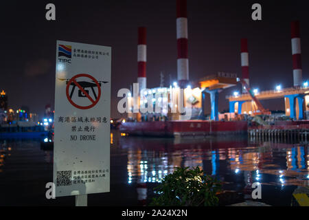 A ' No Drone ' Sign in chinese forbidding to fly Drones with a Industrial Harbor Area in the background at night. No Fly Zone Stock Photo