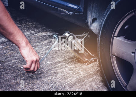 Man lifting car with jack screw for tire changing   of punctured wheel -  tire change oncept Stock Photo