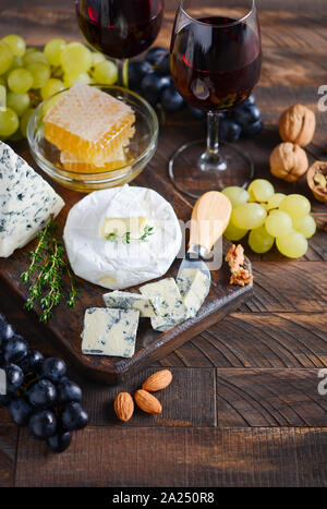 Cheese plate with grapes, honey, nuts and red wine on a wooden table. Stock Photo