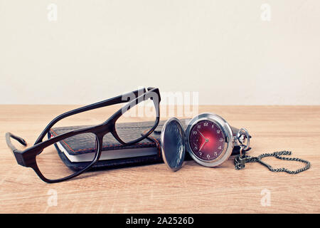 Close up shot of an antique pocket watch with glasses and a planner on a wooden background. Time for time travel. Stock Photo