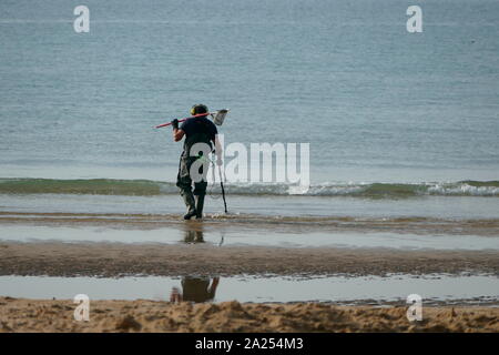 Beachcomber using a metal detector on the south coast of England,   looking for things of value, interest or utility. Stock Photo