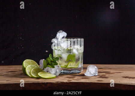 Mojito summer beach refreshing tropical cocktail in glass with splash and drops: soda water, lime juice, mint leaves, sugar, ice and rum on vintage wo Stock Photo