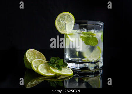 Mojito summer beach refreshing tropical cocktail in glass with soda water, lime juice, mint leaves, sugar, ice and rum on reflective black surface. Stock Photo
