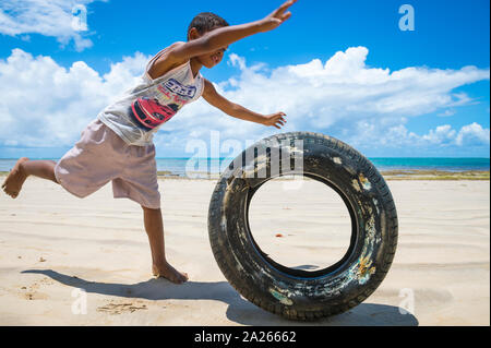 BAHIA, BRAZIL - FEBRUARY 15, 2017: A young Brazilian boy rolls a tire as a game along a an empty beach on a remote island in rural Bahia. Stock Photo