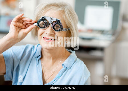 Senior woman checking vision with eye test glasses during a medical examination at the ophthalmological office Stock Photo