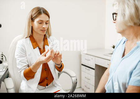 Senior woman patient talking with female ophthalmologist during a medical consultation at the ophthalmologic office. Doctor offering eye medcine for a Stock Photo