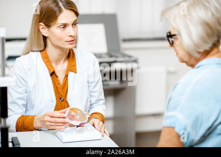 Female ophthalmologist showing the eye model to a senior patient during a medical consultation in the ophthalmologic office Stock Photo