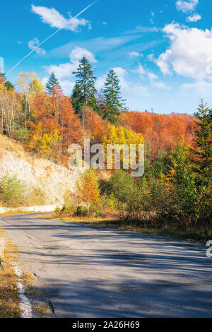 country road through forest in mountains. beautiful transportation autumn scenery in the morning. trees in colorful foliage. old cracked asphalt surfa Stock Photo