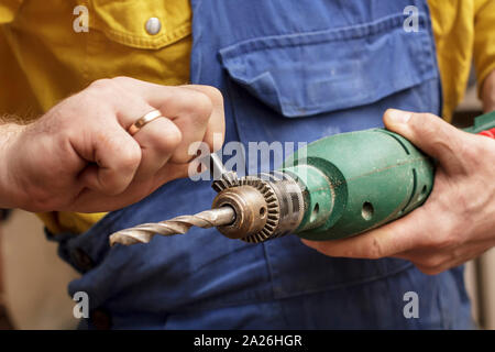 worker man in a blue dress and yellow shirt inserts a bit in a drill using hands Stock Photo