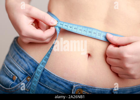 fair-skinned woman in blue jeans is measured using a tape beautiful slender waist Stock Photo