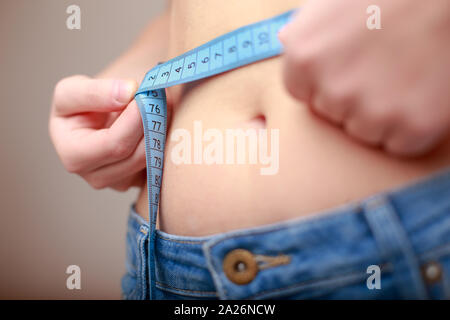 fair-skinned woman in blue jeans is measured using a tape beautiful slender waist Stock Photo