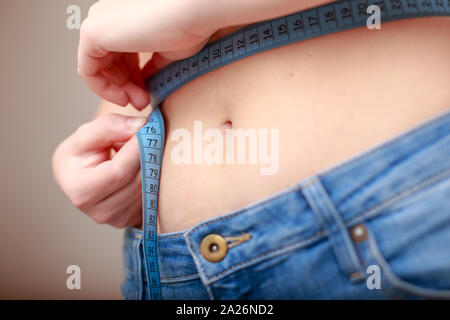 fair-skinned woman in blue jeans is measured using a tape beautiful slender waist Stock Photo