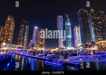 Dubai marina skyline at night with boats in the harbor, United Arab Emirates