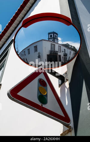 White facade of the house in the background. Traffic mirror reflecting a building and a traffic sign - street lights. Ribeira Grande, Sao Miguel, Azor Stock Photo