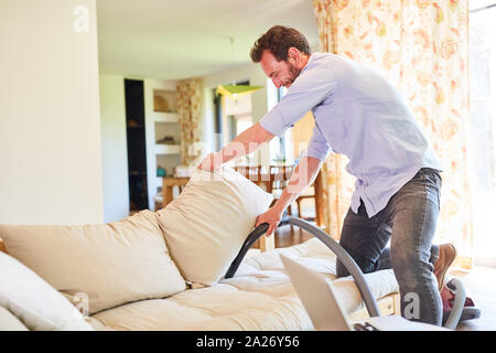 Houseman in the living room vacuuming on the couch during spring cleaning Stock Photo