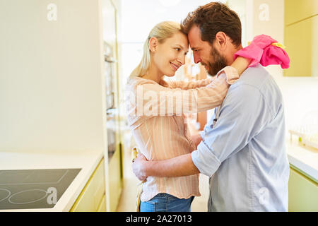 Happy couple hugging while doing housework or cleaning their dishes in the kitchen Stock Photo