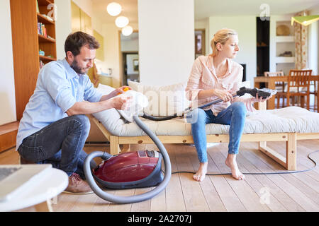 Young couple with vacuum cleaner in the living room is doing spring cleaning together Stock Photo
