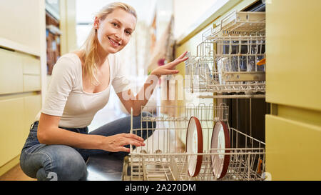 Smiling housewife or maid at the dishwasher in the kitchen Stock Photo