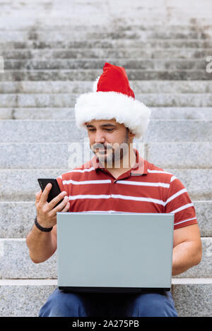 man with santa claus hat using laptop and smartphone Stock Photo